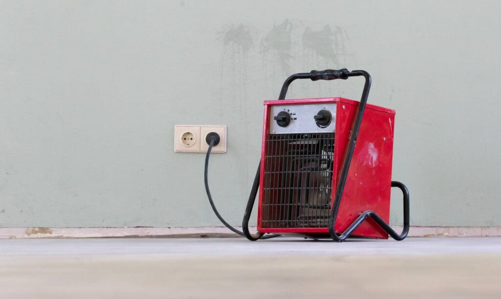 Red portable electric heater plugged into a wall outlet on a bare floor.