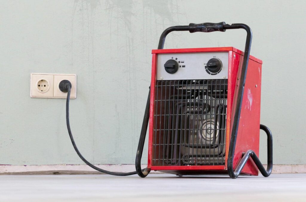 Red portable electric heater plugged into a wall outlet on a light-colored floor.